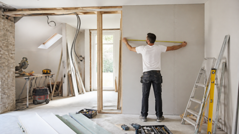 Intérieur d'une maison en rénovation avec un ouvrier mesurant un mur